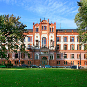 Eine Fotografie vom Hauptgebäude der Rostocker Universität - im Vordergrund ist grüner Rasen zu sehen, im Hintergrund das prunkvolle Gebäude